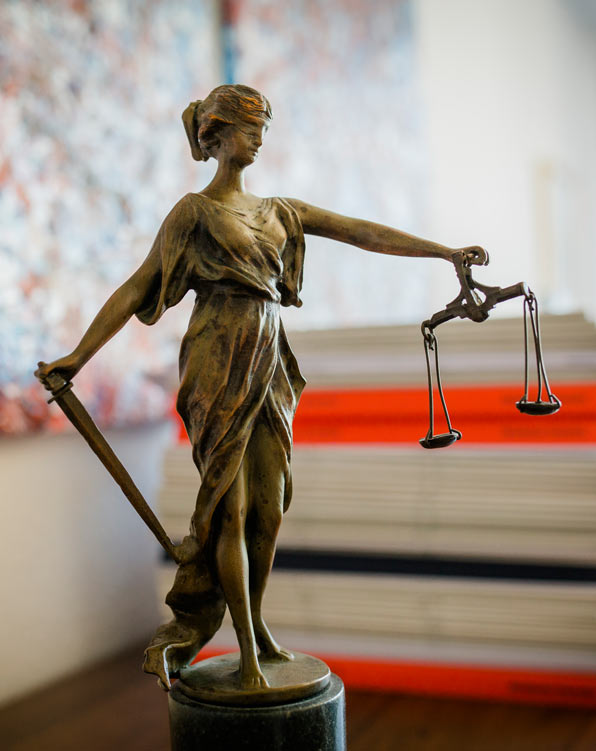 Justitia-Figur vor einem Stapel mit Unterlagen